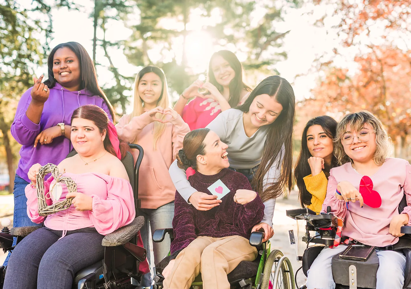 Nine joyful women, including wheelchair users, celebrate friendship in a vibrant autumn park.