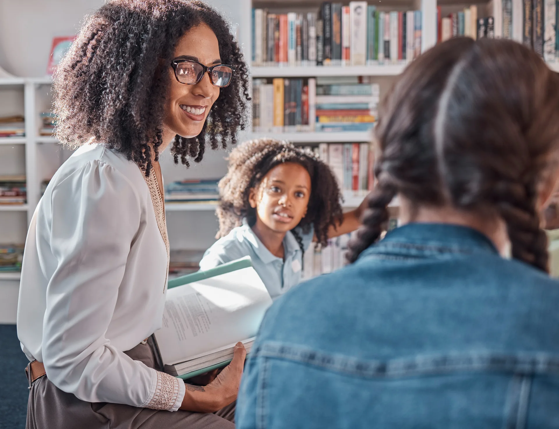 Three people sharing a book in a cozy library setting, engaged in warm conversation.