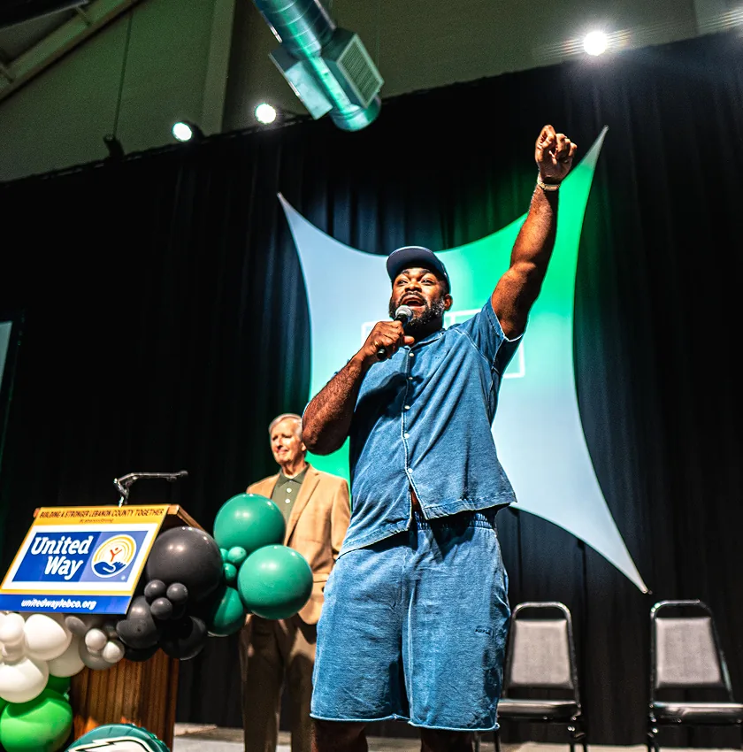 Black speaker raises fist while addressing crowd at political rally stage.