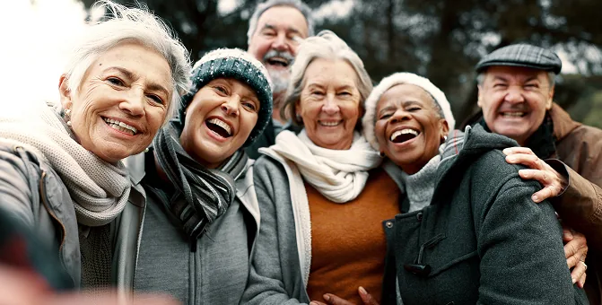 Six joyful seniors smile together outdoors in warm, cozy winter attire.