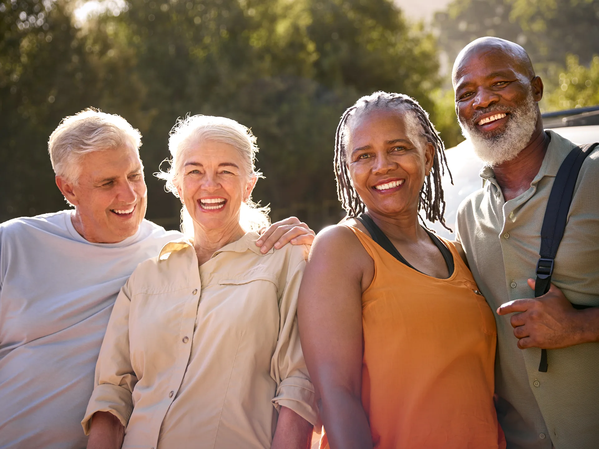 Four joyful senior friends smiling together in a sunlit park.