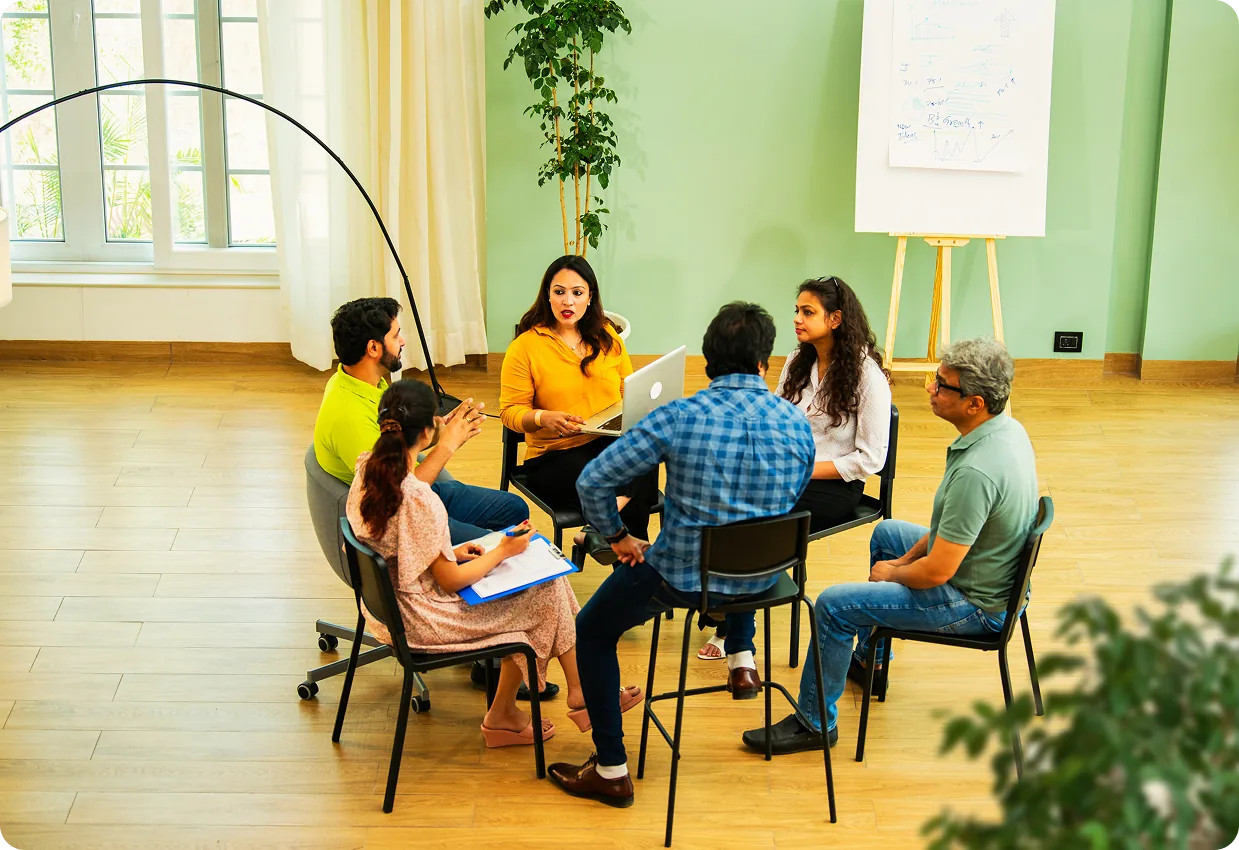 Six people in a circle discussing in a bright, modern meeting room.